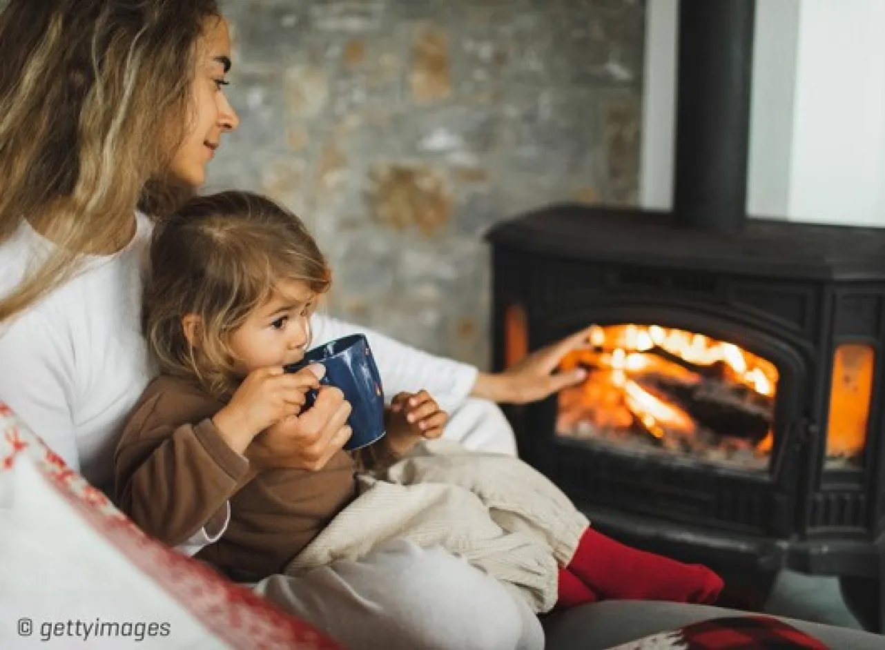 Femme avec un enfant sur ses genoux devant le poêle